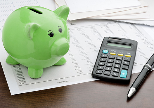 green piggy bank on a office desk next to a calculator and note pad